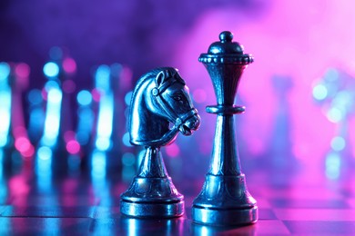Photo of Queen and knight on chessboard in color light, selective focus