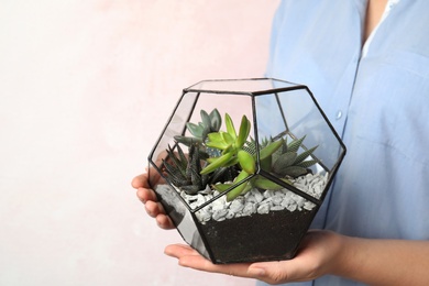 Woman holding florarium with different succulents on color background, closeup. Space for text