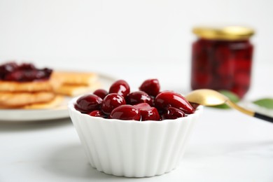 Photo of Delicious dogwood jam with berries in bowl on white table, closeup