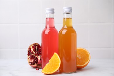 Photo of Delicious kombucha in glass bottles, pomegranate and orange on white table