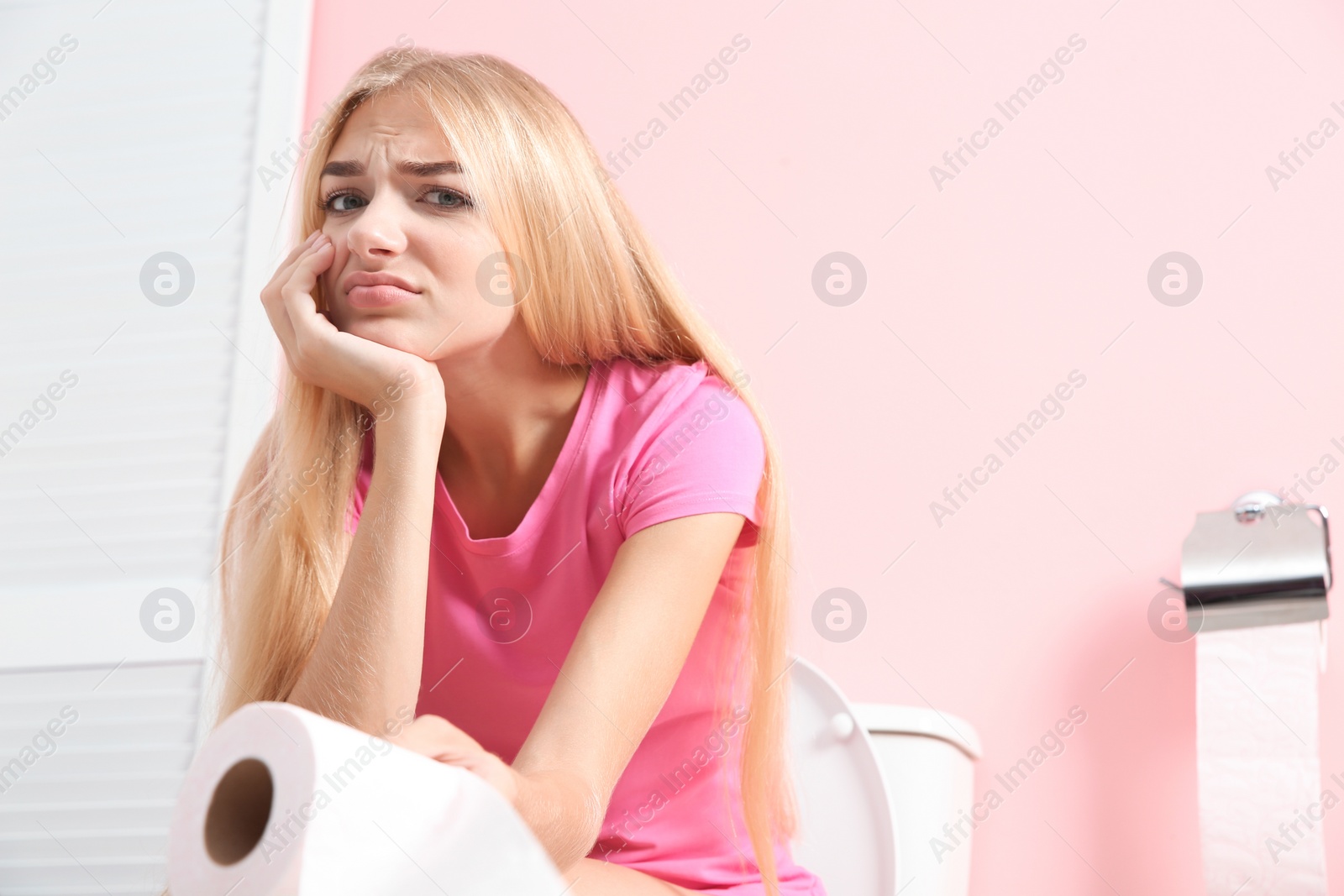 Photo of Woman with paper roll sitting on toilet bowl in bathroom