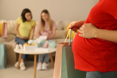 Photo of Pregnant woman holding shopping bags in room with her friends, closeup
