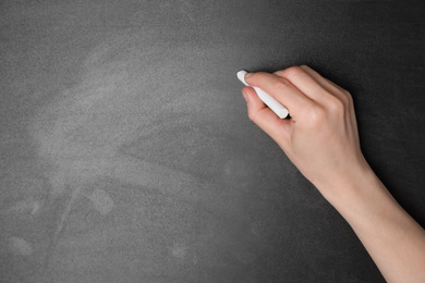 Photo of Woman with white chalk near blackboard, closeup. Space for text