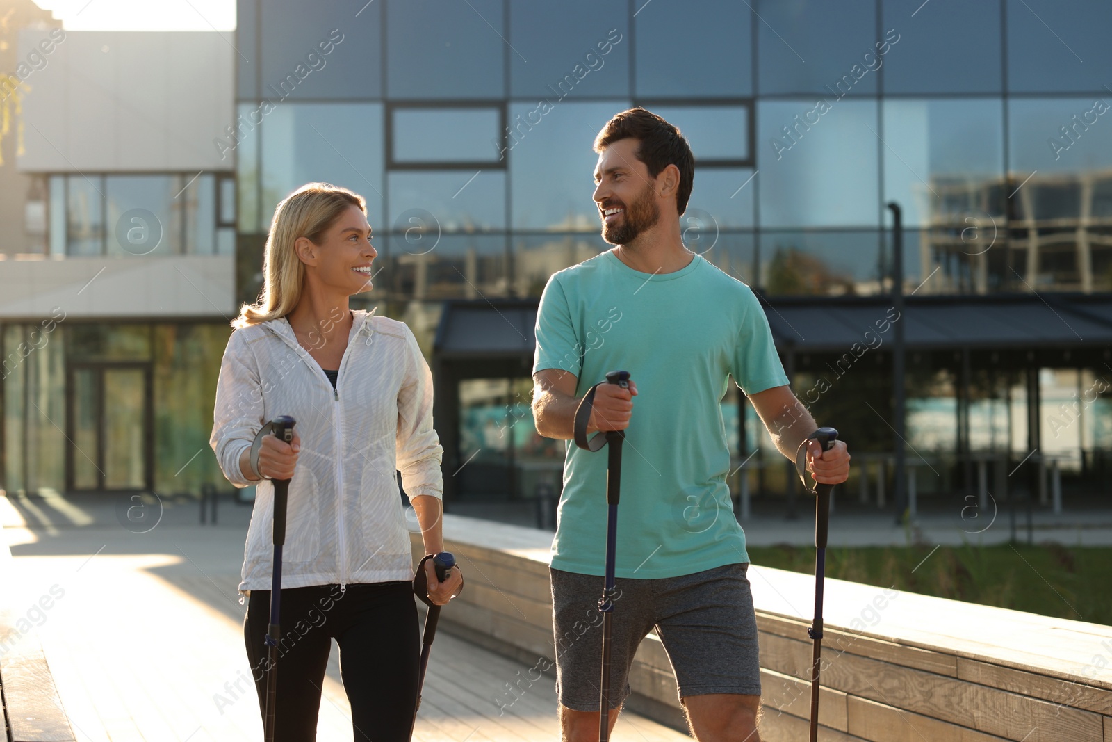 Photo of Happy couple practicing Nordic walking with poles outdoors