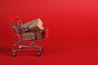 Photo of Small metal shopping cart with cardboard boxes on red background, space for text
