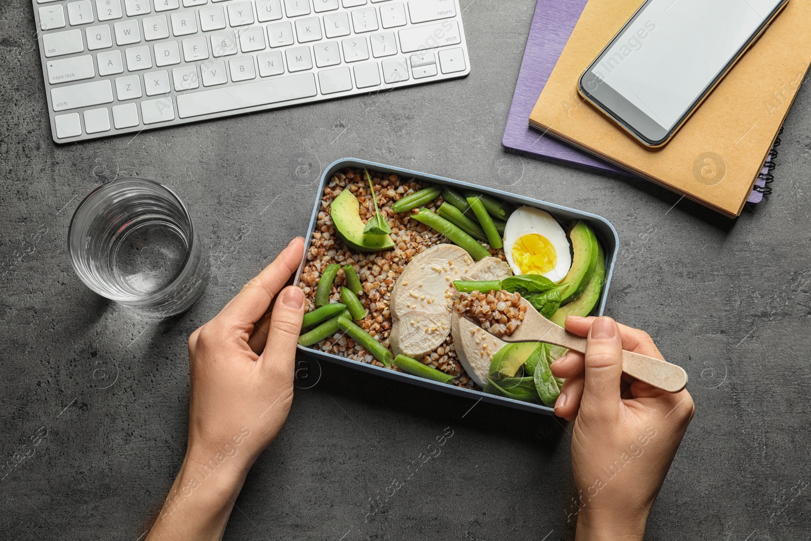 Photo of Woman eating natural protein food from container at office table, top view