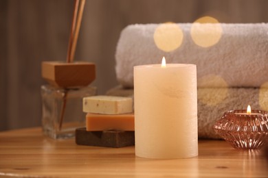 Photo of Spa composition. Burning candles, towels, soap and reed air freshener on wooden table, closeup