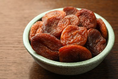 Photo of Bowl of tasty apricots on wooden table, closeup. Dried fruits