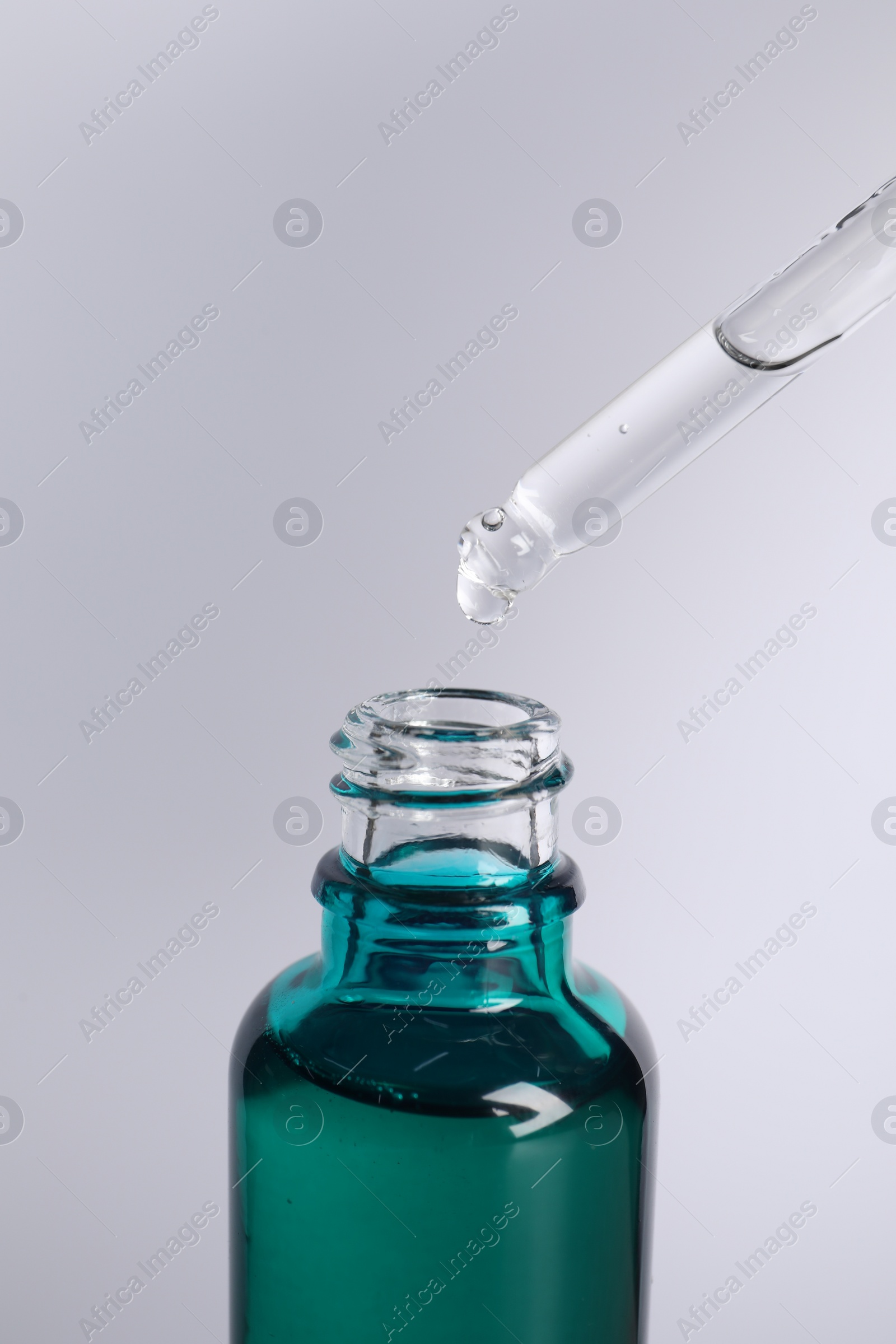 Photo of Dripping cosmetic serum from pipette into bottle on light grey background