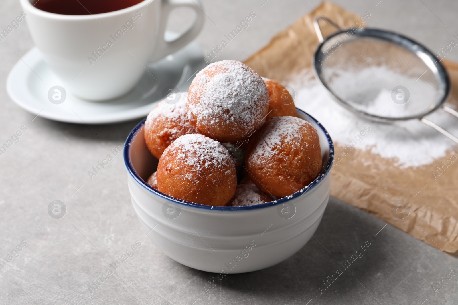 Photo of Delicious sweet buns in bowl, cup of drink and strainer on gray table