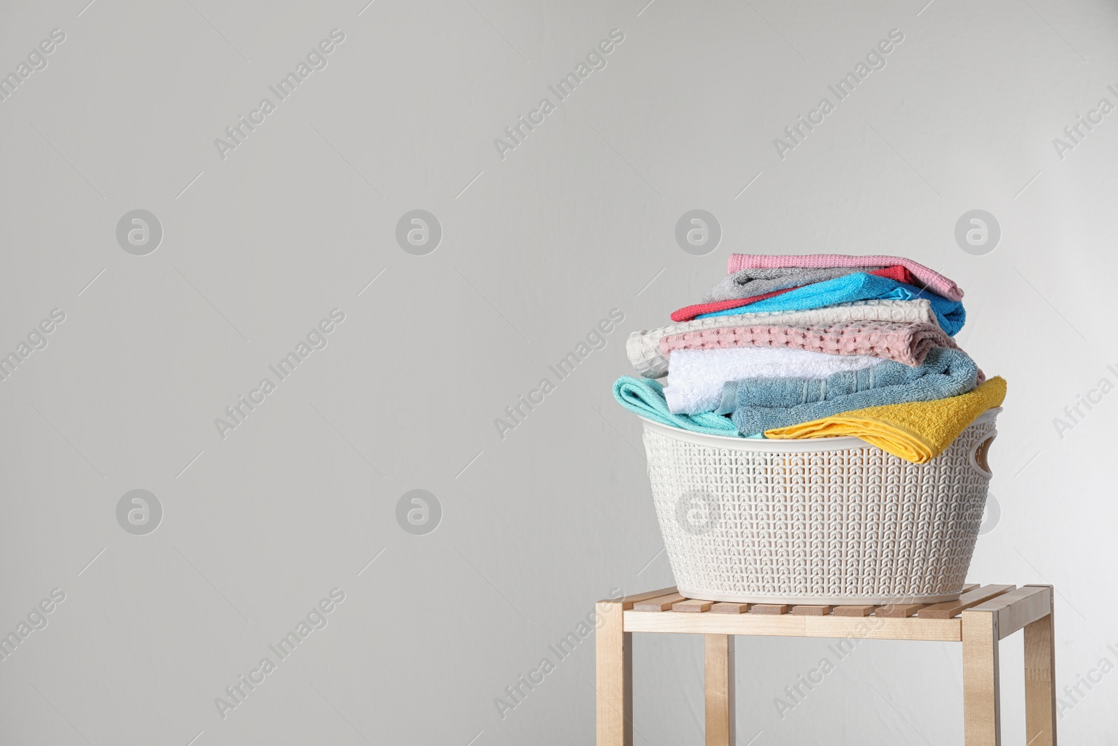 Photo of Laundry basket with clean towels on table against light background. Space for text