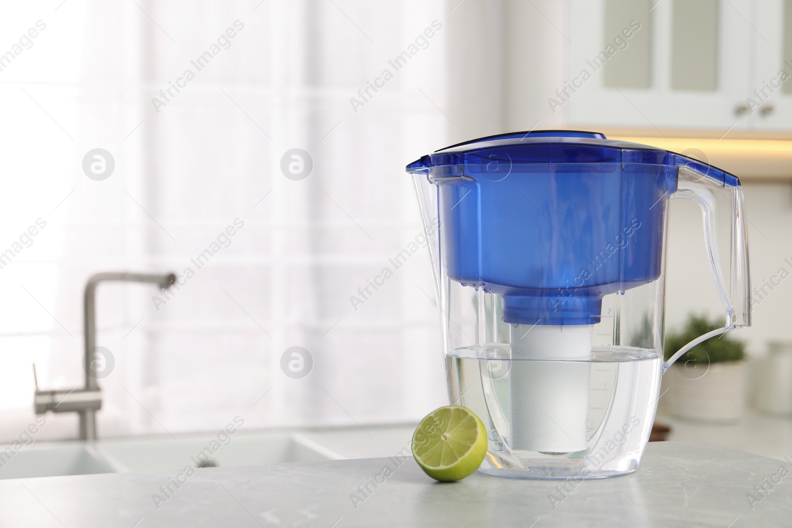 Photo of Water filter jug and lime on light table in kitchen. Space for text