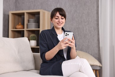 Photo of Beautiful young housewife using smartphone on sofa at home