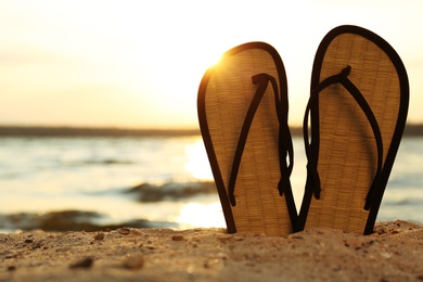 Photo of Stylish flip flops on sand near sea, space for text. Beach accessories