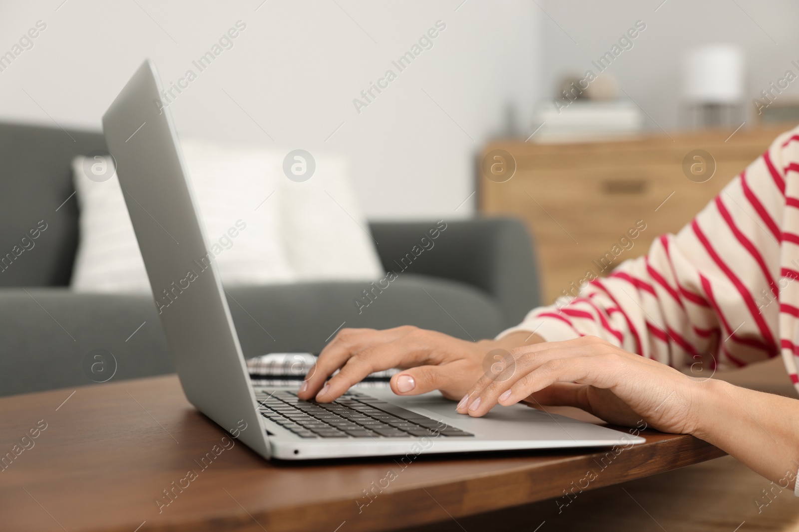 Photo of Woman using laptop at wooden coffee table in room, closeup