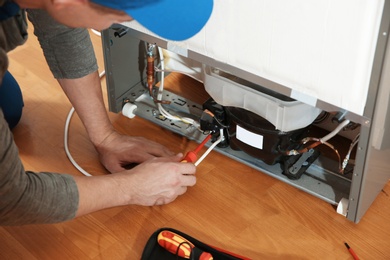 Male technician repairing broken refrigerator indoors, closeup