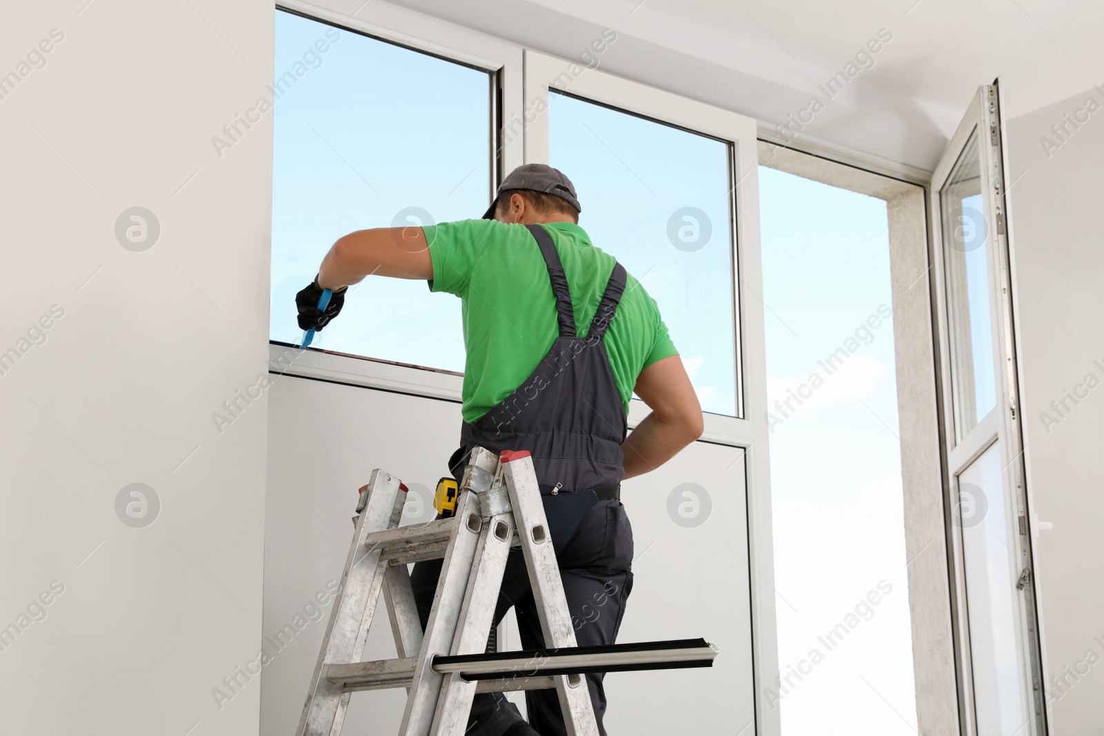 Photo of Worker on folding ladder installing window indoors