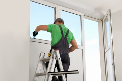 Photo of Worker on folding ladder installing window indoors