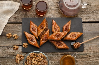 Photo of Delicious sweet baklava with walnuts, honey and hot tea on wooden table, flat lay