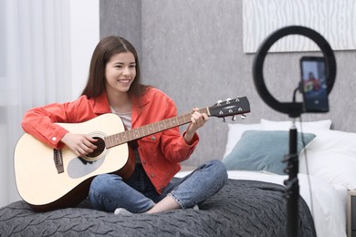 Photo of Smiling teenage blogger playing guitar while streaming at home