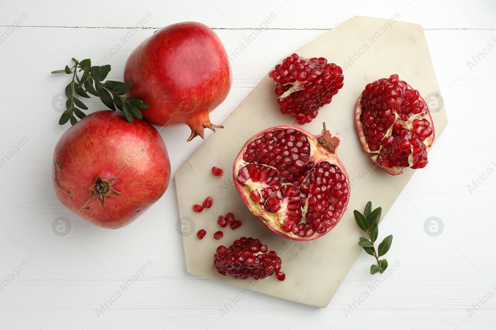 Photo of Fresh pomegranates and branches on white wooden table, flat lay