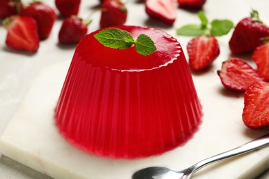 Photo of Stone board with fruit jelly, strawberries and spoon on light table