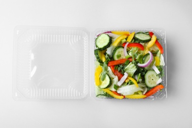 Plastic container with fresh salad on white background, top view