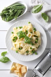 Photo of Delicious pasta with green peas and fresh basil on white wooden table, flat lay