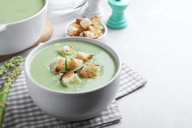 Photo of Bowl of delicious asparagus soup served on light grey table, space for text