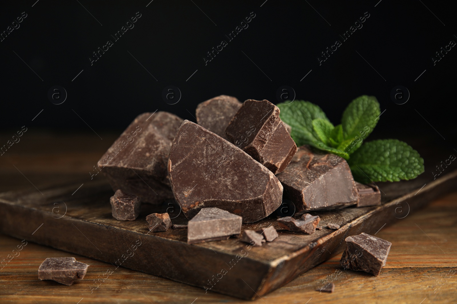 Photo of Tasty dark chocolate pieces with mint on wooden table
