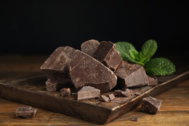 Photo of Tasty dark chocolate pieces with mint on wooden table