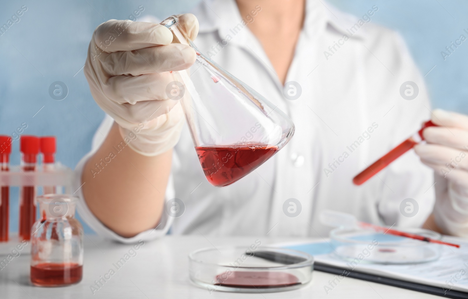 Photo of Scientist holding conical flask and tube with blood samples at table, closeup. Virus research