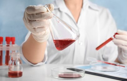 Photo of Scientist holding conical flask and tube with blood samples at table, closeup. Virus research