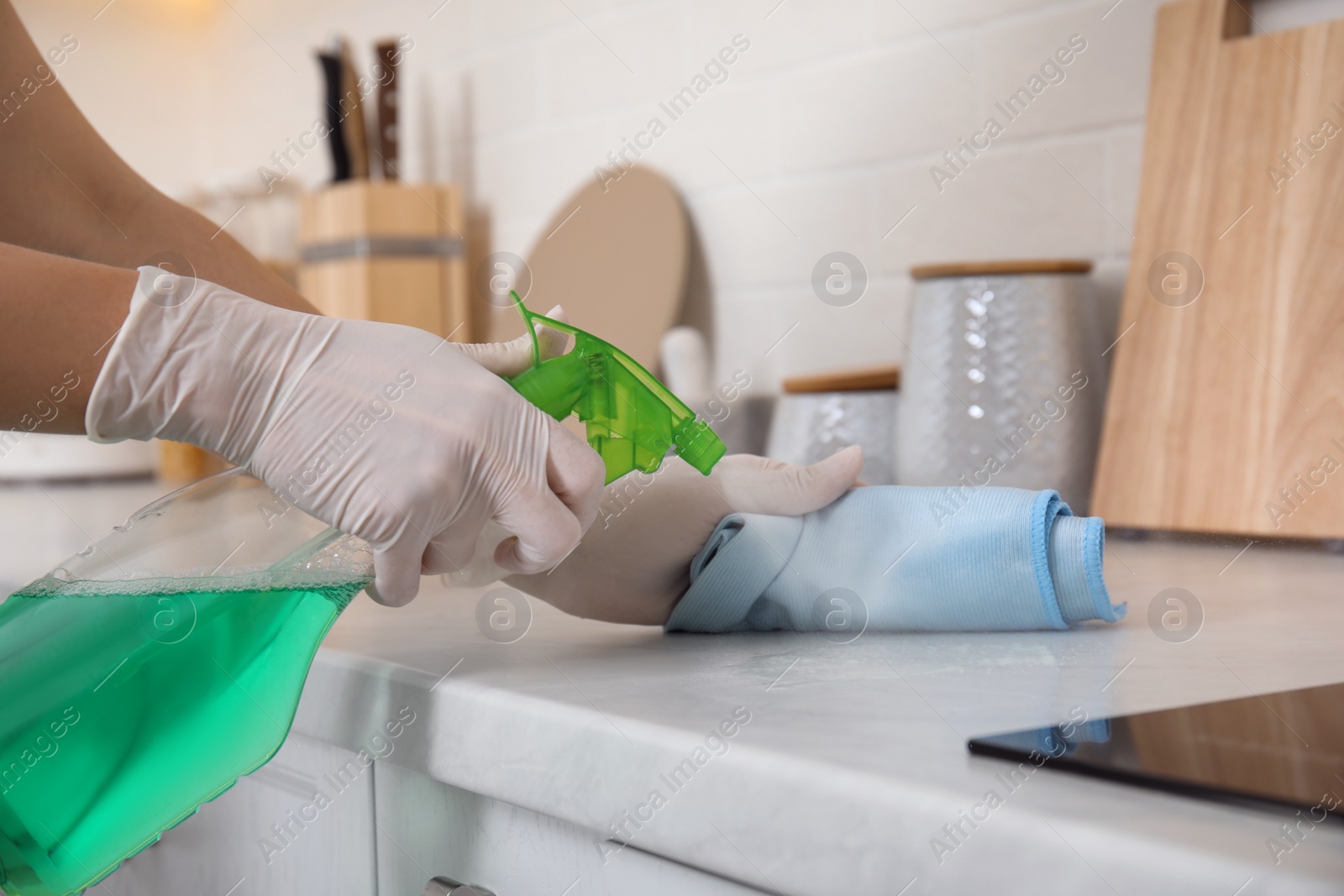 Photo of Woman cleaning white marble countertop with rag and detergent in kitchen, closeup