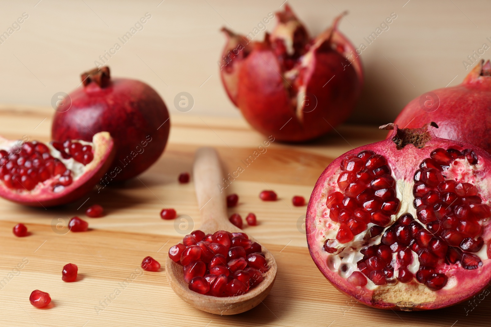 Photo of Composition with ripe pomegranates and spoon of seeds on wooden table