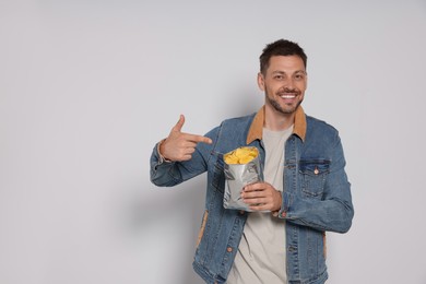 Handsome man pointing on potato chips against light grey background. Space for text