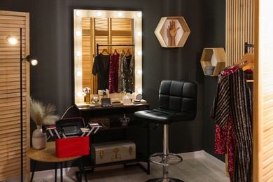 Makeup room. Stylish mirror near dressing table with beauty products and chair indoors