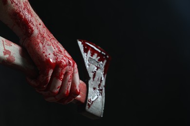 Photo of Man holding bloody axe on black background, closeup. Space for text