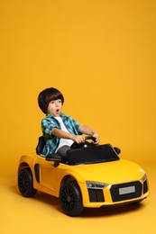 Photo of Cute little boy driving children's electric toy car on yellow background