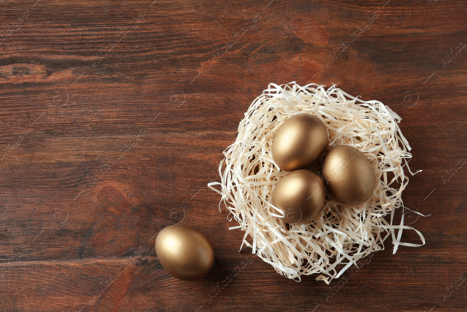 Photo of Nest with golden eggs on wooden background, top view. Space for text