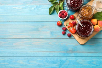 Photo of Jars with different jams and fresh fruits on light blue wooden table, flat lay. Space for text