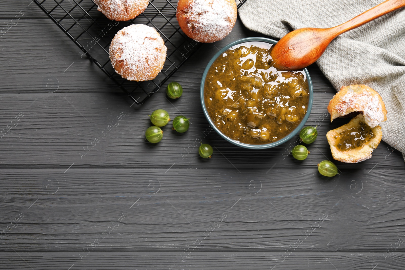 Photo of Delicious gooseberry jam, fresh berries and buns on grey wooden table, flat lay. Space for text