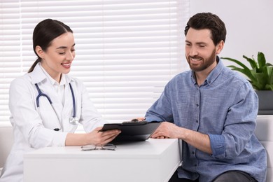 Photo of Doctor with clipboard consulting patient during appointment in clinic