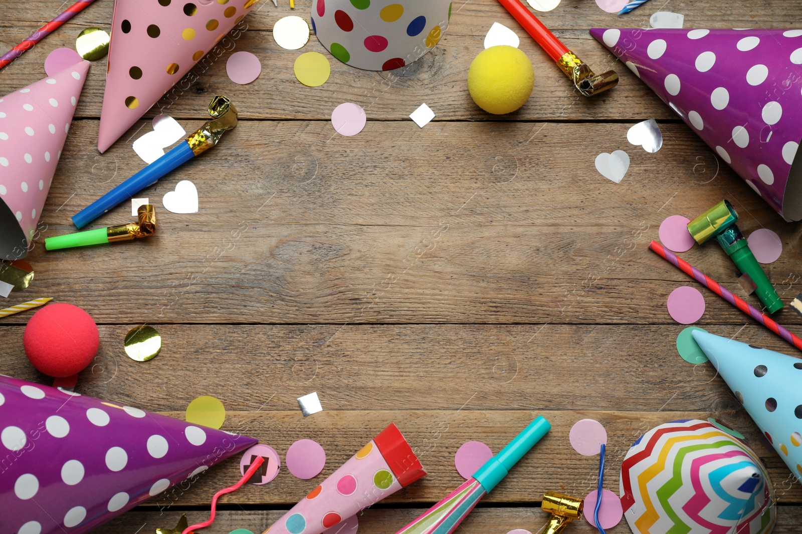 Photo of Frame made of colorful party hats and other festive items on wooden table, flat lay. Space for text