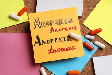 Photo of Sticky note with words Anorexia and pills on cork board surface, flat lay