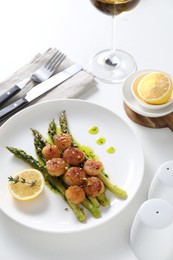 Delicious fried scallops with asparagus, lemon and thyme served on white table