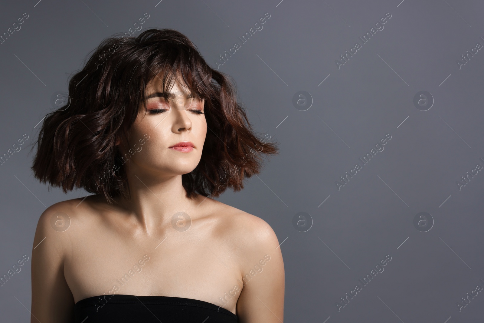 Photo of Portrait of beautiful young woman with wavy hairstyle on grey background. Space for text