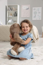 Cute little girl with teddy bear on floor at home