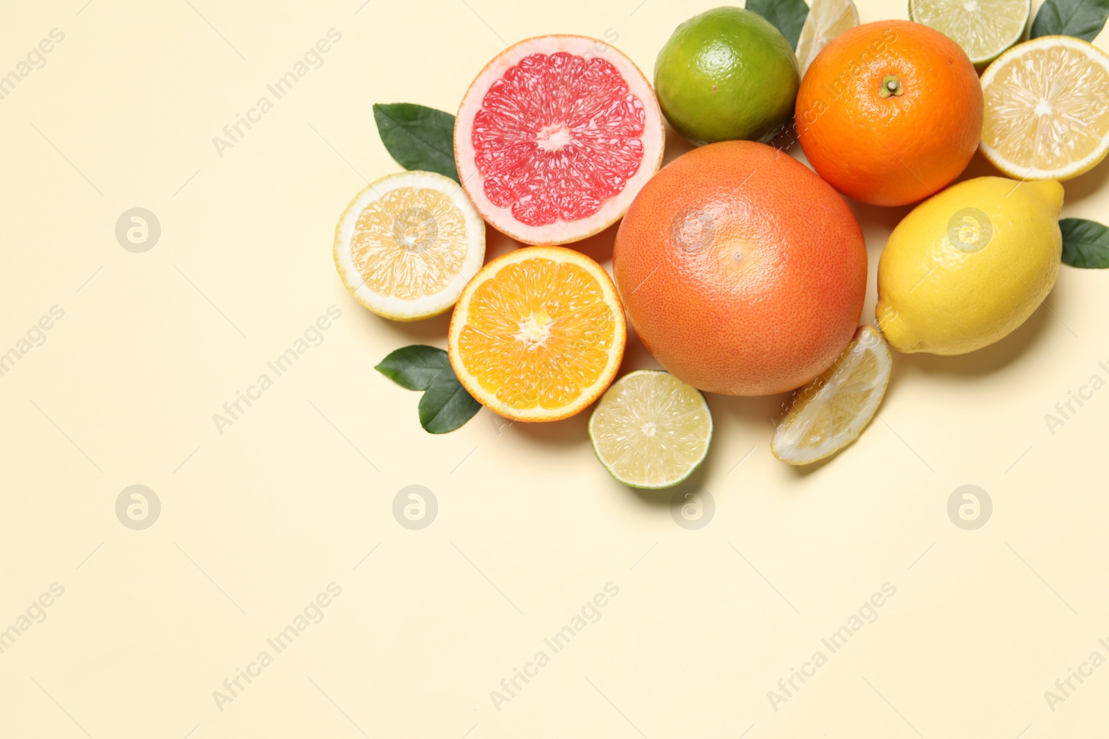 Photo of Different cut citrus fruits and leaves on beige table, flat lay. Space for text