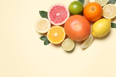 Different cut citrus fruits and leaves on beige table, flat lay. Space for text